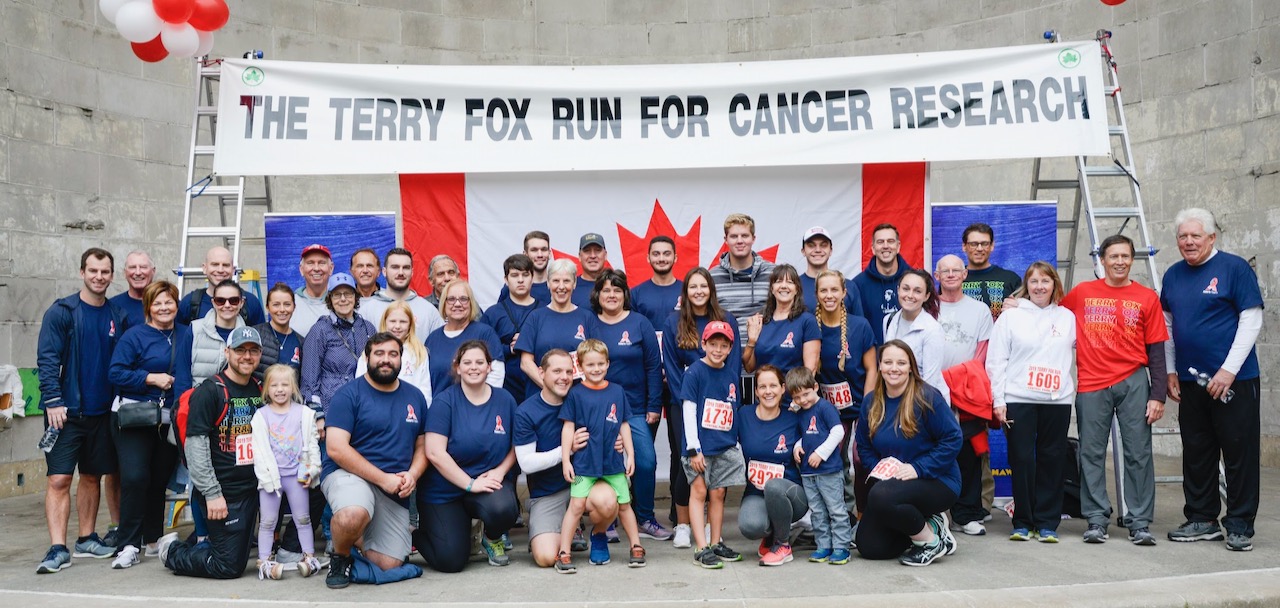 A crowd of about twenty-five people pose smiling at the Terry Fox Run event in Central Park